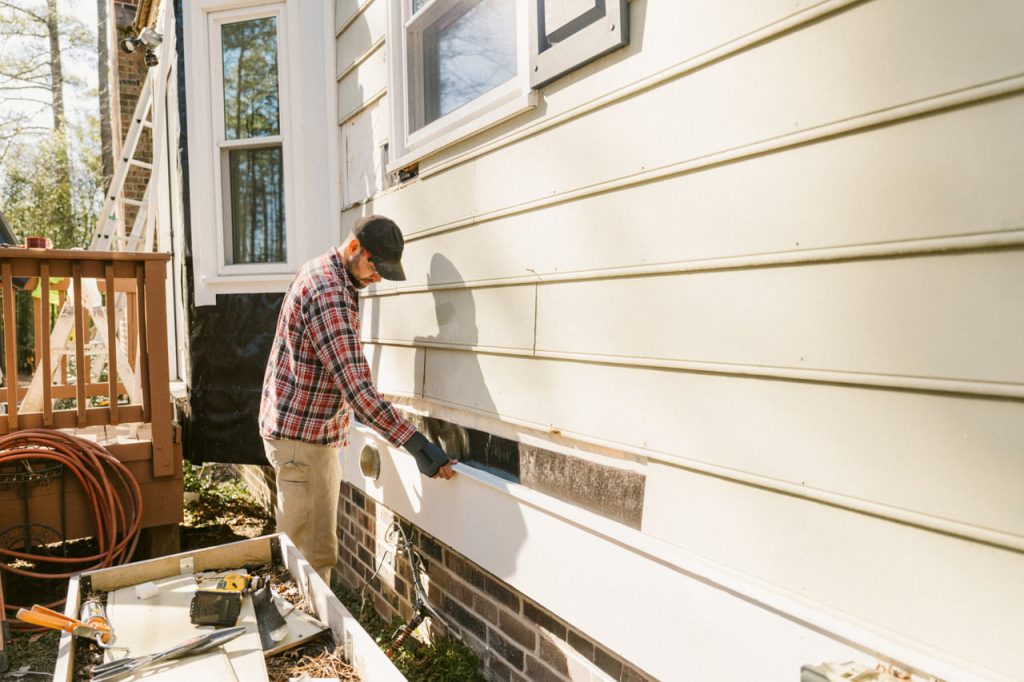 A man replacing a strip of composite siding on a home.